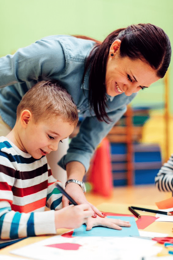 A woman helping a child with crafts in a classroom.